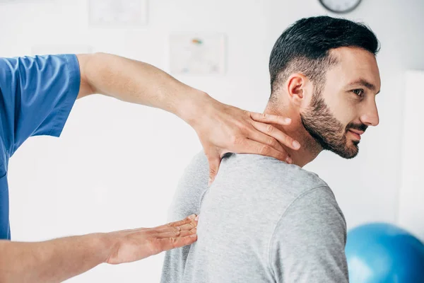 Quiroprático massageando pescoço de homem bonito no hospital — Fotografia de Stock