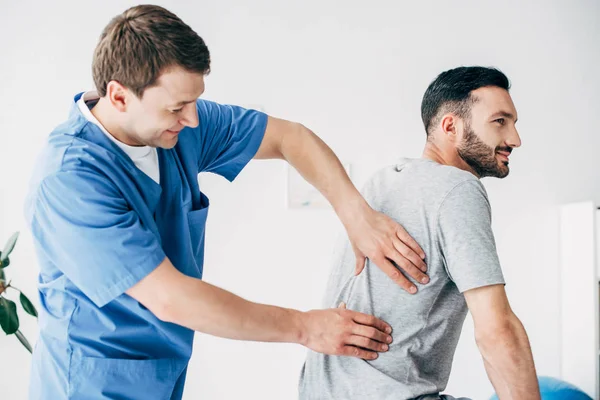 Quiropráctico masajeando la espalda de un hombre guapo en el hospital - foto de stock