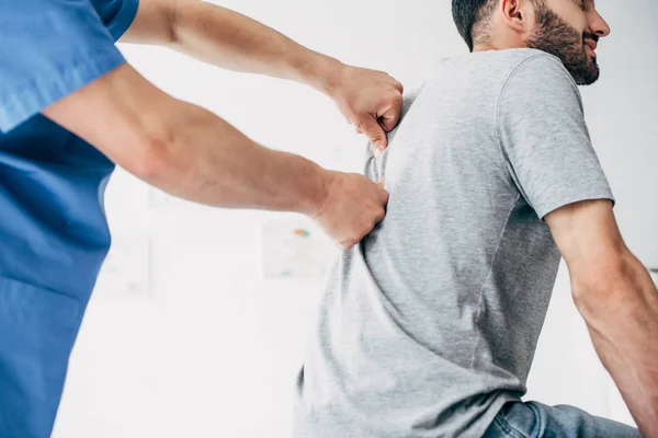 Fisioterapeuta masajeando la espalda del hombre barbudo en el hospital - foto de stock