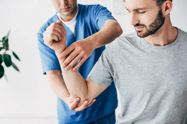 Physiotherapist massaging arm of handsome patient in hospital — Stock Photo