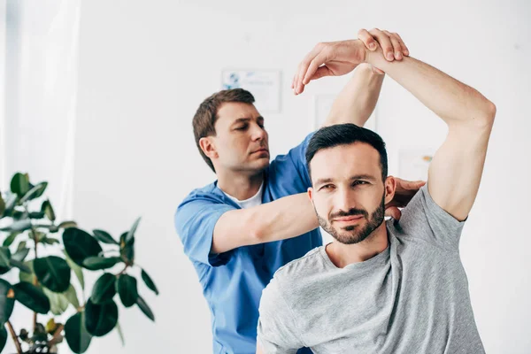 Chiropractor stretching arm of handsome patient in hospital — Stock Photo