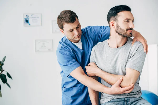 Physiotherapist massaging arm of handsome patient in hospital — Stock Photo