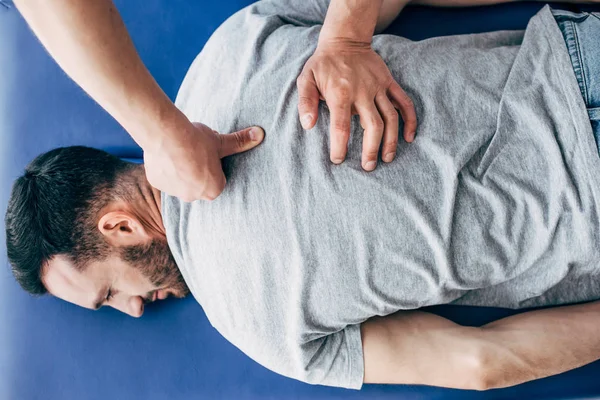 Vista superior de Fisioterapeuta masajeando la espalda del hombre acostado en la mesa de masaje en el hospital - foto de stock