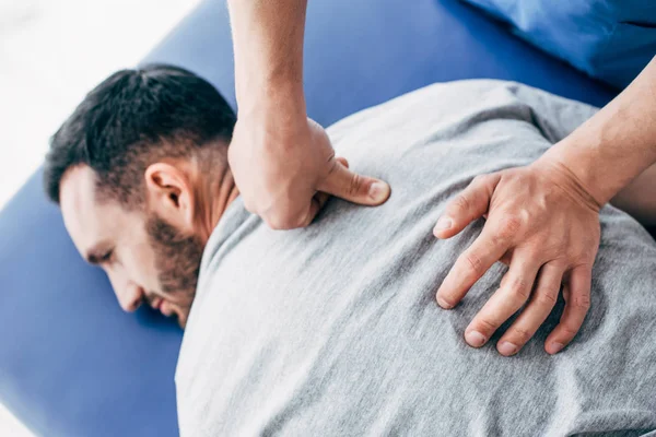 Physiotherapeut massiert Rücken eines auf Massagetisch liegenden Mannes im Krankenhaus — Stockfoto