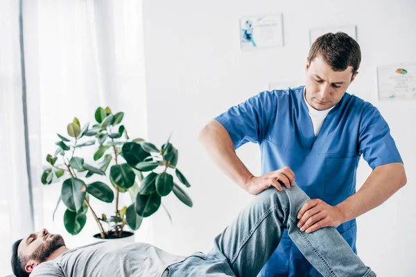Handsome Physiotherapist massaging leg of patient in hospital — Stock Photo