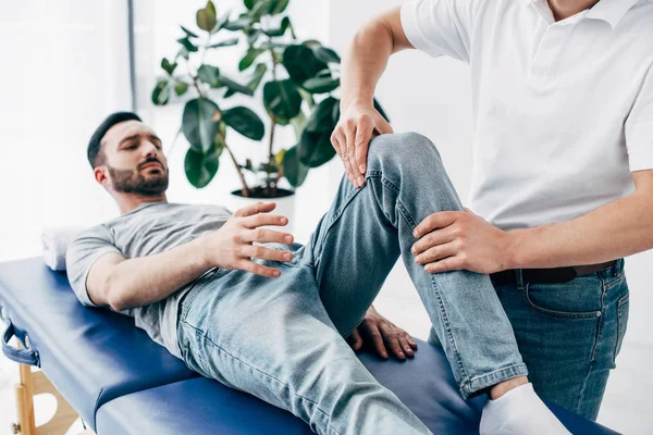 Physiotherapeut massiert Bein einer Patientin, die im Krankenhaus auf Massagetisch liegt — Stockfoto