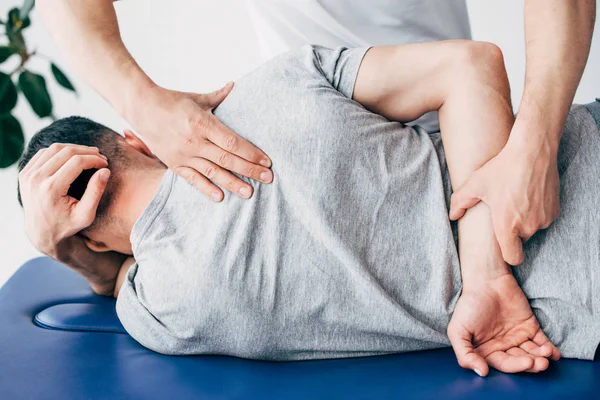 Vista posterior del quiropráctico masajeando la espalda del hombre acostado en la mesa de masaje en el hospital - foto de stock