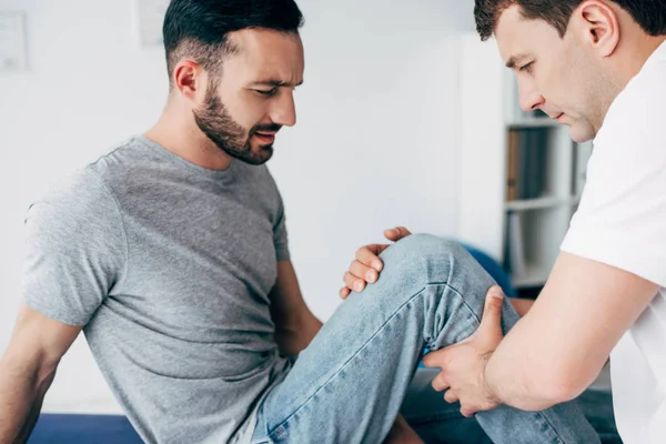 Handsome Physiotherapist massaging leg of good-looking patient in hospital — Stock Photo