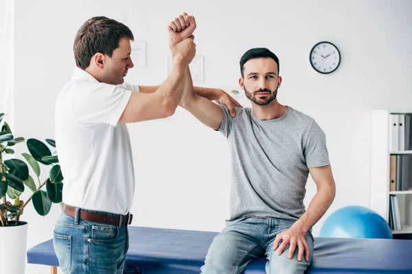 Chiropractor stretching arm of handsome patient on massage table in hospital — Stock Photo