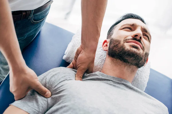 Chiropraktiker massiert Schulter eines auf Massagetisch liegenden Mannes im Krankenhaus — Stockfoto