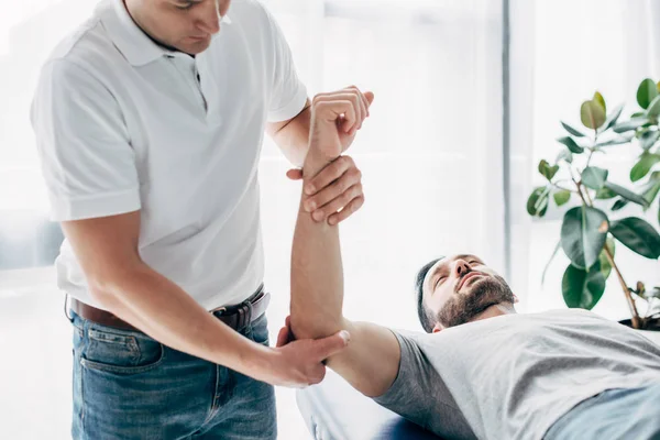 Physiothérapeute étirant le bras du patient barbu à l'hôpital — Photo de stock