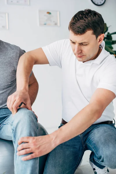 Schöner Physiotherapeut im weißen Hemd massiert Bein einer Patientin im Krankenhaus — Stockfoto