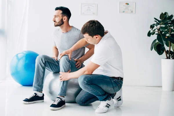 Fisioterapista massaggiare gamba del paziente seduto sulla palla fitness in ospedale — Foto stock