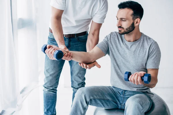 Chiropractor stretching arm of handsome patient with dumbbells in hospital — Stock Photo