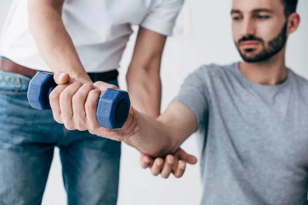 Chiropractor stretching arm of patient with dumbbell on grey — Stock Photo