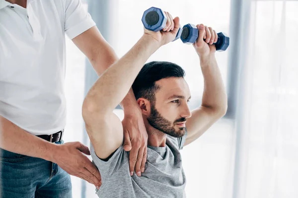 Chiropractor massaging shoulder of patient holding dumbbells in hospital — Stock Photo