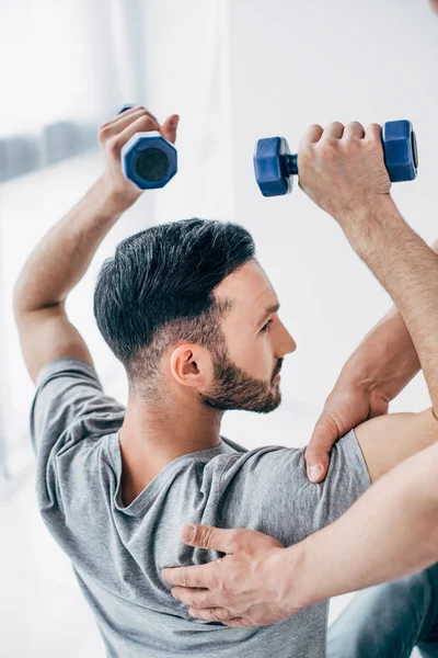 Chiropractor massaging shoulder of patient holding dumbbells in hospital — Stock Photo