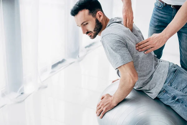 Chiropraktiker massiert Rücken eines gutaussehenden Mannes, der auf Fitnessball liegt — Stockfoto