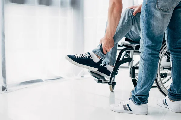 Vue recadrée du physiothérapeute massant la jambe du patient en fauteuil roulant à l'hôpital — Photo de stock