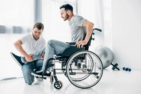 Fisioterapeuta masajeando pierna de hombre discapacitado en silla de ruedas - foto de stock