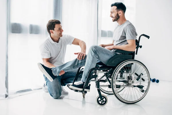 Fisioterapista sorridente che massaggia la gamba dell'uomo handicappato in sedia a rotelle — Foto stock