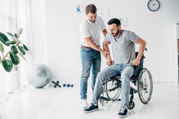 Physiothérapeute aidant l'homme en fauteuil roulant pendant la récupération à l'hôpital — Photo de stock