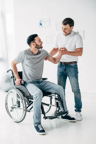 Fisioterapeuta ayudando al hombre discapacitado en silla de ruedas durante la recuperación en el hospital - foto de stock