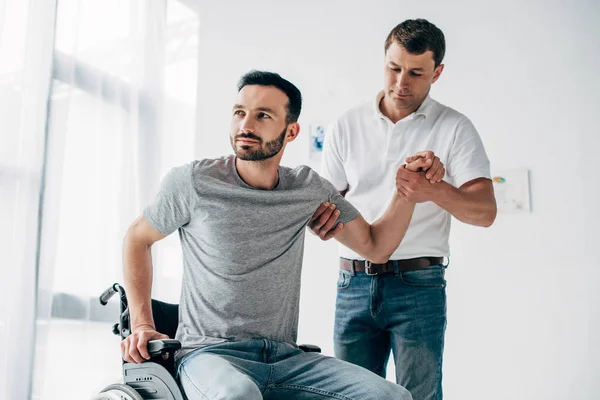 Physiotherapist helping handicapped man in Wheelchair during recovery — Stock Photo