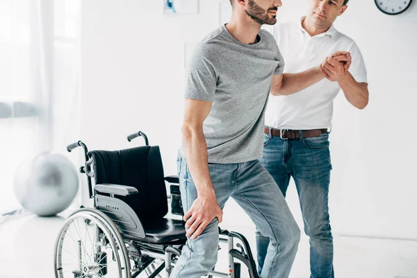 Vista recortada del fisioterapeuta ayudando al hombre discapacitado durante la recuperación - foto de stock