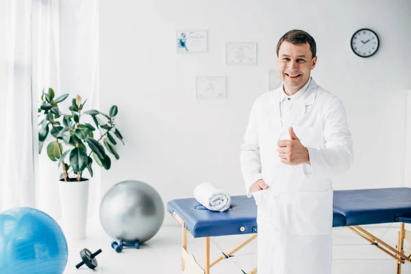 Good-looking smiling chiropractor showing thumb up in hospital — Stock Photo
