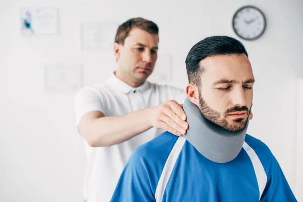 Chiropractor examining good-looking football player in neck brace in hospital — Stock Photo
