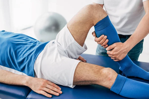 Vista recortada de Fisioterapeuta masaje pierna de jugador de fútbol en el hospital - foto de stock