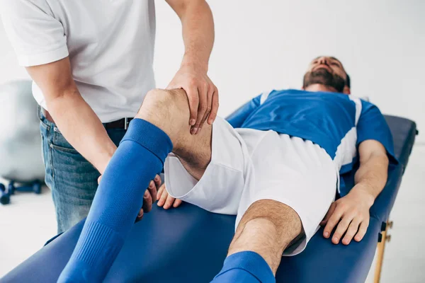 Fisioterapista massaggiare gamba di giocatore di calcio in ospedale — Foto stock
