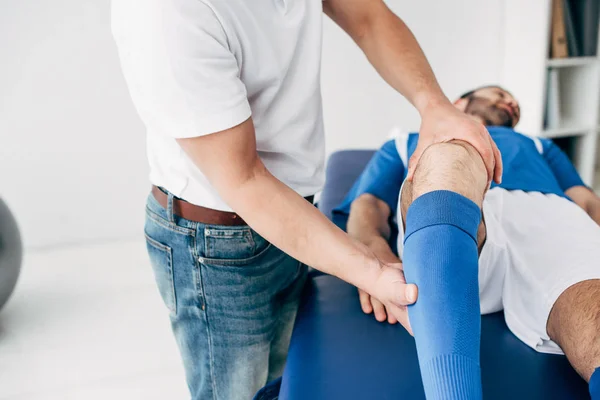Fisioterapista massaggiare gamba di giocatore di calcio sul lettino da massaggio in ospedale — Foto stock