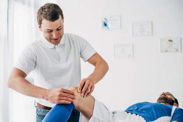 Schöne Physiotherapeutin massiert Bein eines Fußballers im Krankenhaus — Stockfoto