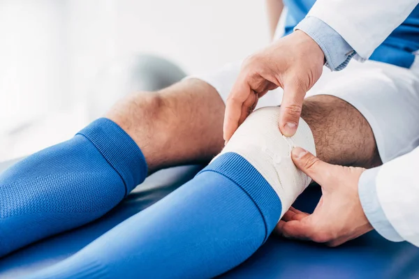 Частичный взгляд физиотерапевта, накладывающего упругую повязку на ногу футболиста — стоковое фото