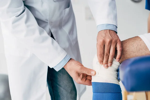 Частичный взгляд физиотерапевта, накладывающего упругую повязку на ногу футболиста — стоковое фото