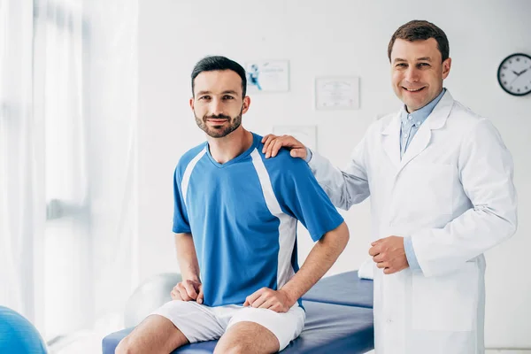 Smiling Physiotherapist and football player in hospital looking at camera — Stock Photo