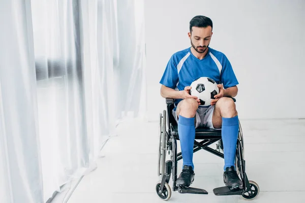 Uomo in uniforme da calcio seduto sulla sedia a rotelle e con in mano palla da calcio — Foto stock