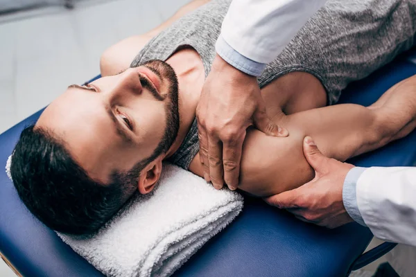 Хіропрактик масажує плече красивого чоловіка на масажному столі в лікарні — стокове фото