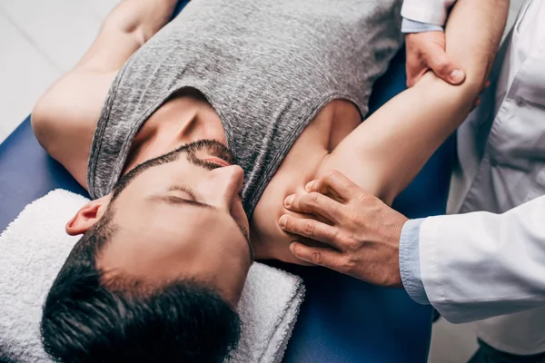 Quiropráctico masajeando hombro de hombre en mesa de masaje en el hospital - foto de stock