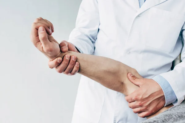 Cropped view of chiropractor stretching arm of patient on grey — Stock Photo