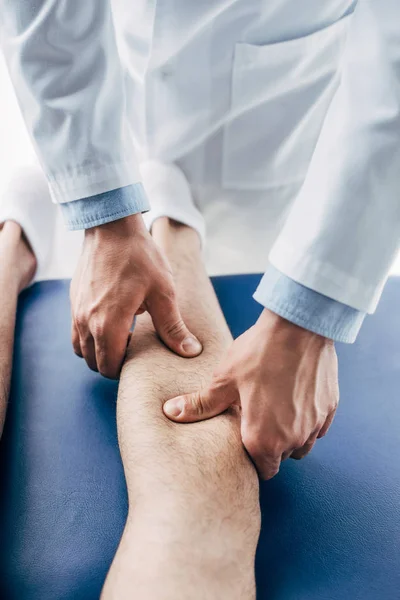 Vue crêpée de physiothérapeute massant jambe de l'homme à l'hôpital — Photo de stock