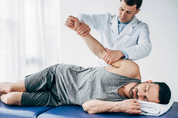 Braccio stiramento chiropratico di bel paziente sdraiato sul lettino da massaggio in ospedale — Foto stock