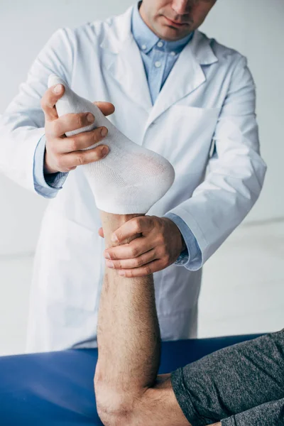 Vista recortada del fisioterapeuta estiramiento de la pierna del paciente en el hospital - foto de stock
