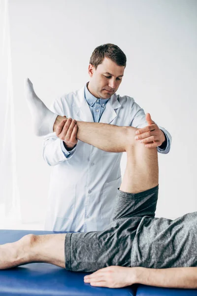Bello fisioterapista stretching gamba del paziente in ospedale — Foto stock