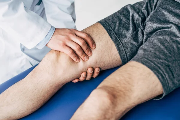 Vue partielle du physiothérapeute massant la jambe de l'homme sur la table de massage à l'hôpital — Photo de stock