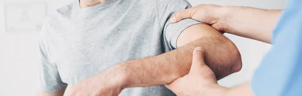 Panoramic shot of chiropractor massaging arm of patient in hospital — Stock Photo