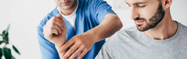 Panoramic shot of chiropractor massaging arm of bearded patient in hospital — Stock Photo