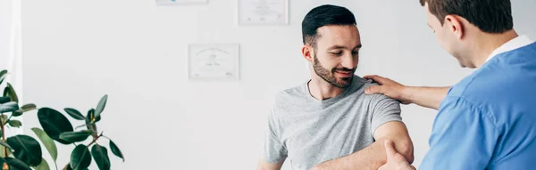 Panoramic shot of chiropractor massaging arm of patient in hospital with copy space — Stock Photo